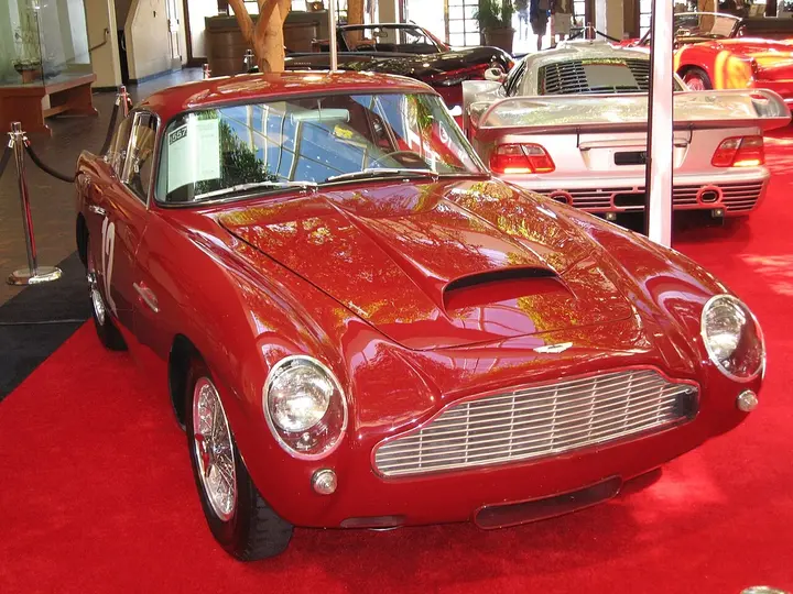 A red 1961 Aston Martin DB4 coupé on a showroom floor